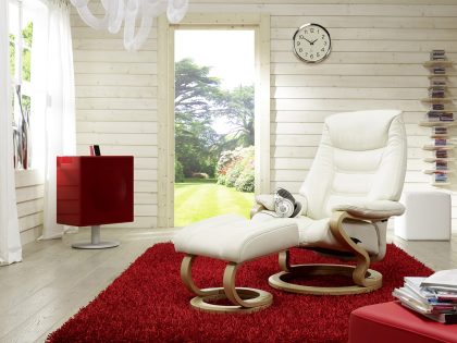A white leather and wood armchair with matching footstool on a red rug in a white wood panel room.