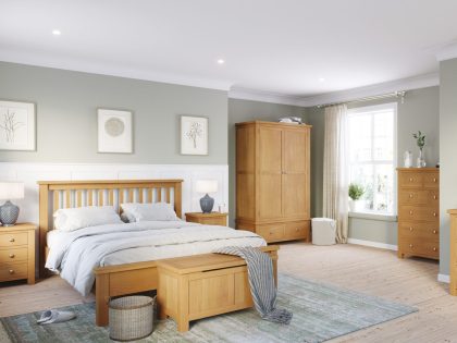 Bedroom with king size bed, bedside chest, blanket box, wardrobe, and tall chest of drawers, all in oak wood colour.