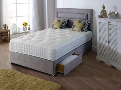 A light grey divan set with uncovered mattress showing an open storage drawer in the divan base, in a bedroom setting.