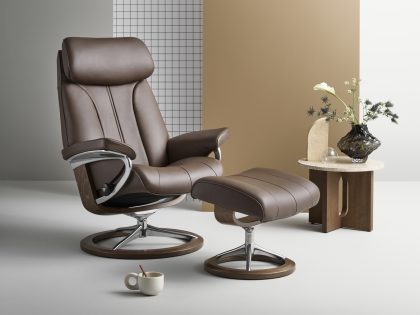 A brown leather recliner chair with matching footstool, both with a circular wooden ring base and silver metal supports.