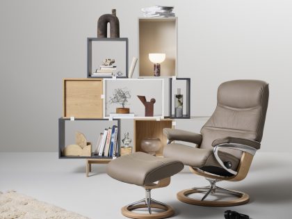 A dark taupe leather recliner chair with matching footstool accompanied by a rug and open box shelving unit.