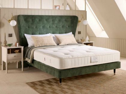 An uncovered mattress sitting on a green fabric bed frame with large buttoned headboard, in a bedroom that has wood panelling an a natural coloured carpet with rug.