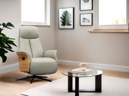 A pale leather high back chair with black star base and wooden side panels, sitting near the corner of a room with a rug and glass coffee table positioned in front of it.