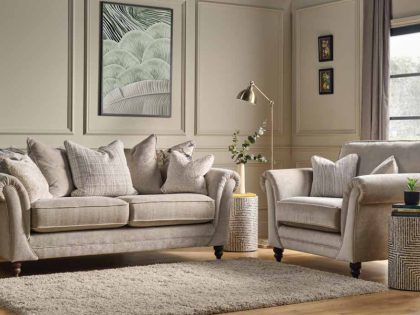A neutral-toned living room showcases a three‑seater sofa and a matching love chair with softly rolled arms and textured cushions, arranged on a plush rug and styled with a floor lamp, side tables, wall art, and large windows that allow natural light to fill the space.