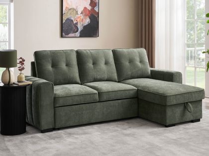 A green fabric chaise sofa positioned in a bright living room, accompanied by a black side table holding a lamp and small plant, with large windows, curtains, wall art, and a potted plant in the background.