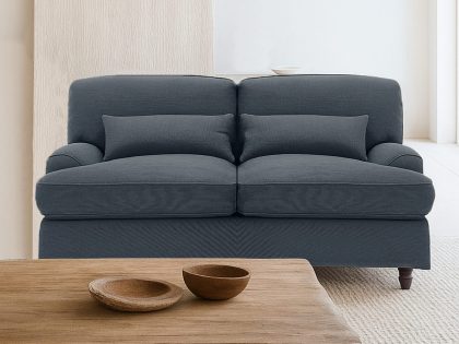 A minimalist living room features a dark blue two-seater sofa positioned behind a low, sculpted wooden coffee table with two wooden bowls, set on a light textured carpet against a soft neutral backdrop.
